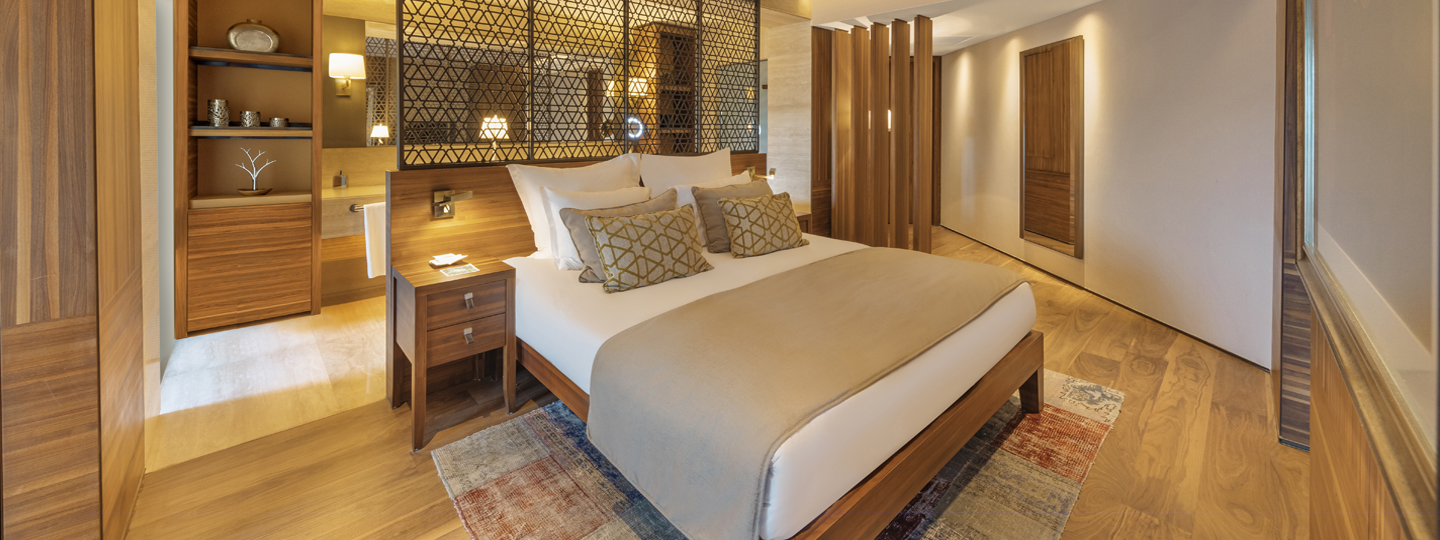 A spacious superior suite at the D Maris Bay resort that opens onto a mountain view. Lush bedroom furnishings open on to modern bathroom facilities, with wooden panelling. 