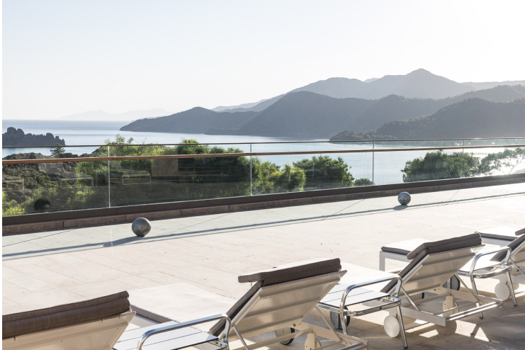 Outdoor sunbeds on the balcony of the Mytha Spa, overlooking a view from D Maris Bay of the unspoiled mountain and sea landscape.