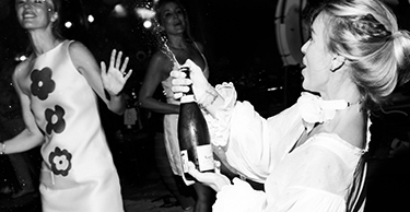A woman pops a champagne cork while others dance in the background, enjoying the nightlife offered at D Maris Bay.