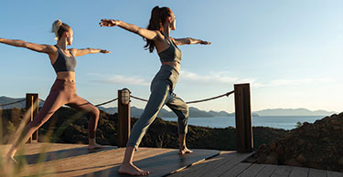 Two women do a warrior pose during a private outdoor yoga class looking out over the scenic landscape at D Maris Bay.